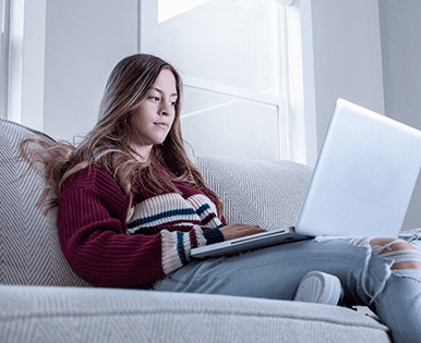teenage girl on computer on couch in home